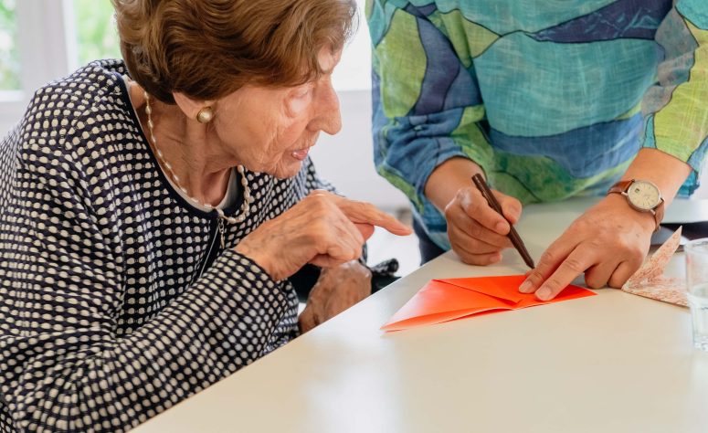 Eine ältere Dame beobachtet eine Falttechnik, die ihr gezeigt wird